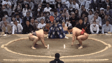 a sumo wrestler is squatting down in front of a crowd while another wrestler stands in front of him