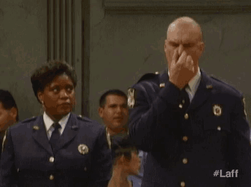 a man in a police uniform is covering his nose with his hand while a group of people watch .