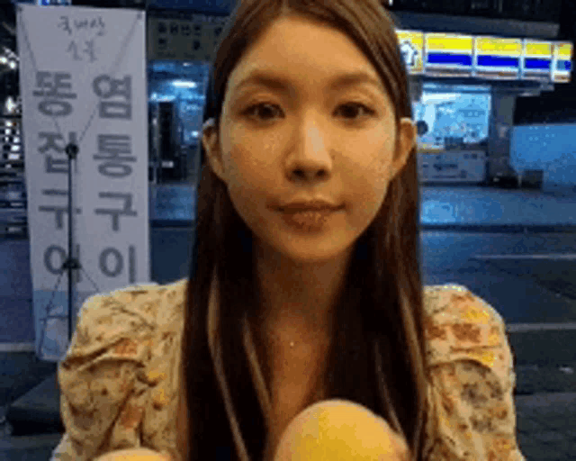 a woman in a floral shirt is holding two oranges in front of a store with chinese writing on it
