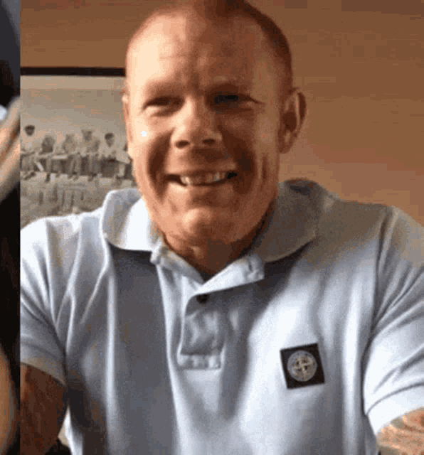a man wearing a light blue shirt with a stone island patch on his chest smiles