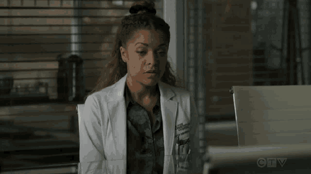 a woman in a lab coat is sitting at a desk using a laptop computer .