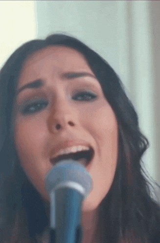 a woman singing into a blue microphone with her mouth open