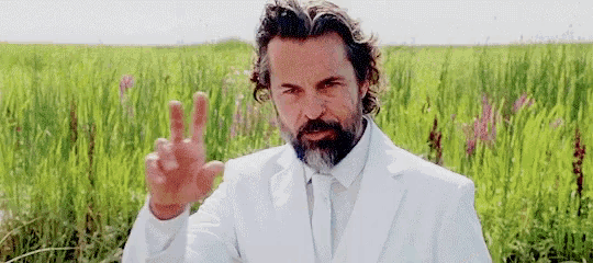 a man with a beard and a white suit is standing in a field of tall grass .