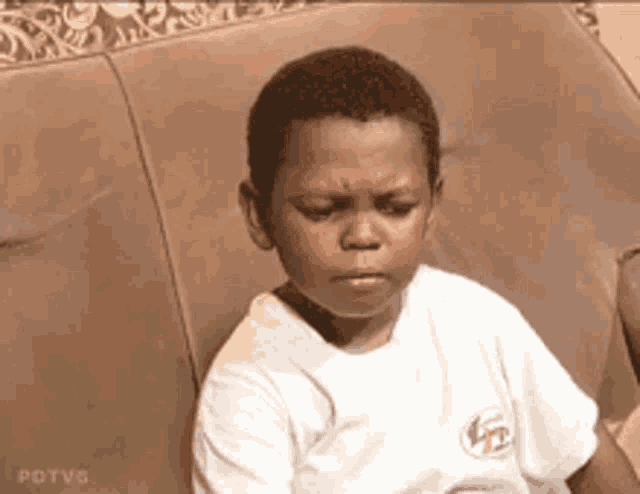a young boy is sitting on a couch with his eyes closed and making a funny face .