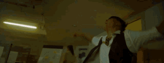 a man in a white shirt and black vest is standing in a dark room and laughing .