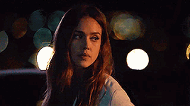 a woman with long brown hair is looking at the camera in a dark room .