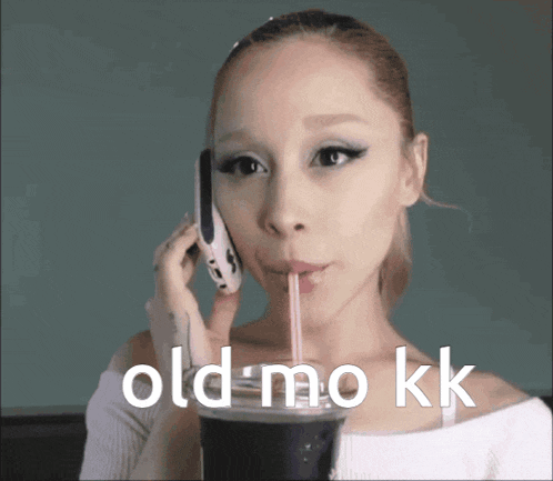 a woman is drinking through a straw while talking on a cell phone with the words old mo kk below her