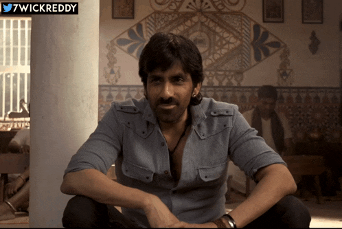 a man in a denim shirt sits in a room with a 7wickreddy sticker on the corner