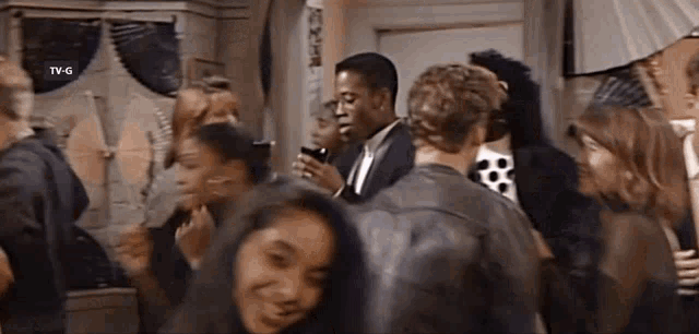 a group of people are standing in a room with a man in a suit talking on a cell phone .