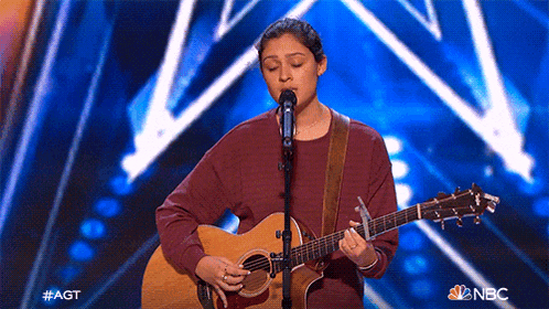a woman singing into a microphone while holding a guitar on stage