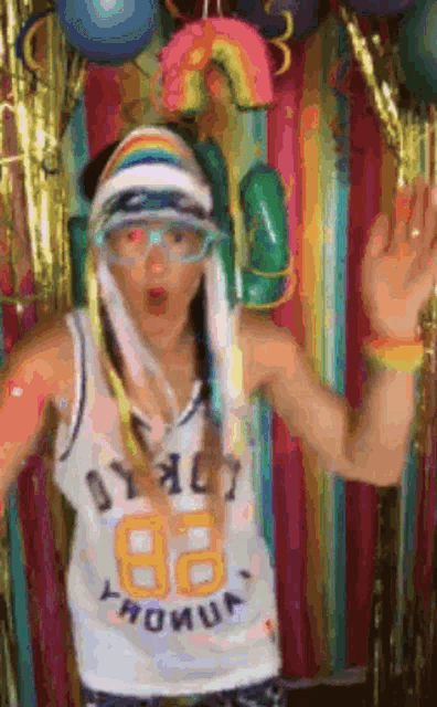 a woman wearing a white tank top with the number 82 on it is standing in front of a colorful background .
