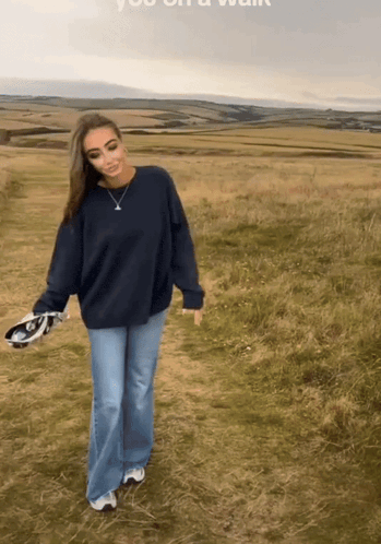 a woman wearing a blue sweater and jeans is walking in a field