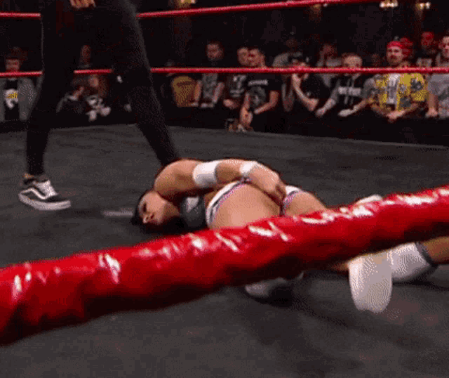 a woman is laying on the ground in a wrestling ring while a referee watches .