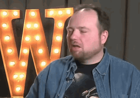 a man with a beard is making a funny face in front of a large w sign .