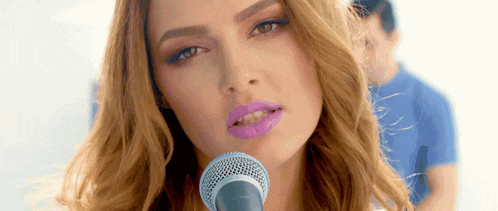 a woman singing into a microphone with purple lipstick on her lips