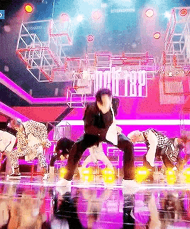 a group of people are dancing on a stage with purple lights .