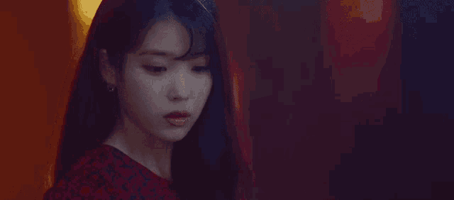 a close up of a woman 's face in a dark room . she is wearing a red dress and earrings .