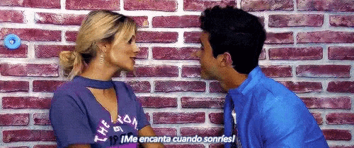 a man and a woman are kissing in front of a brick wall .
