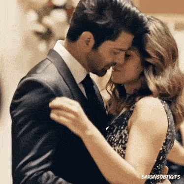 a man in a suit and tie is kissing a woman in a dress while they are dancing .