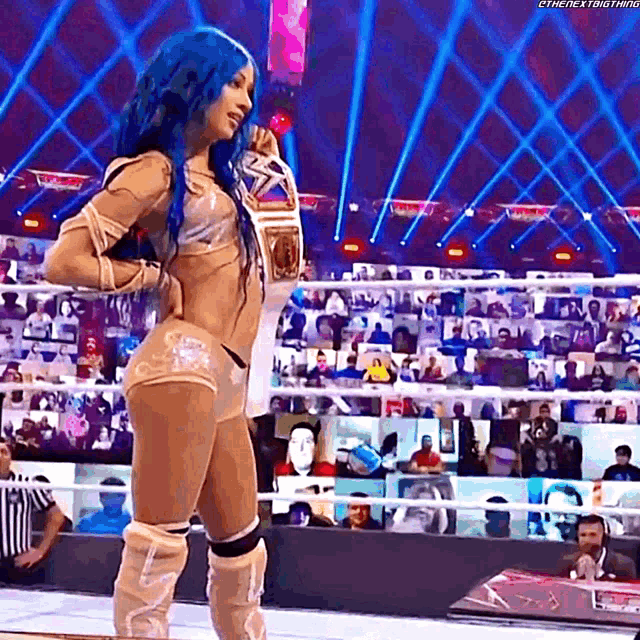 a woman with blue hair is standing in a wrestling ring holding a championship .
