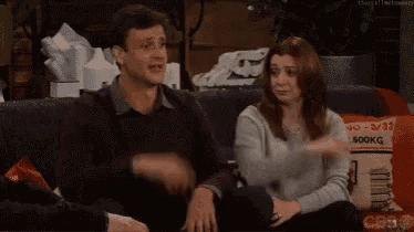 a man and a woman are sitting on a couch . the woman is holding the man 's arm .