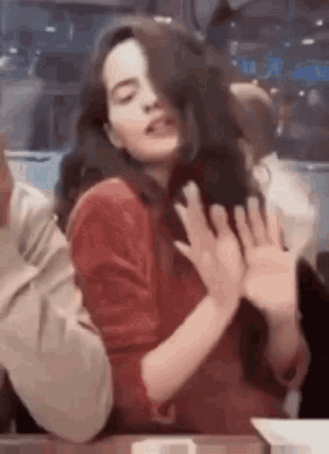 a woman in a red sweater is sitting at a table with her hands on her face .
