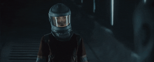 a man wearing glasses and a helmet looks at the camera in a dark room