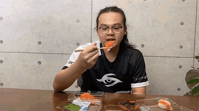 a man is eating sushi with chopsticks while wearing a shirt that says team spirit