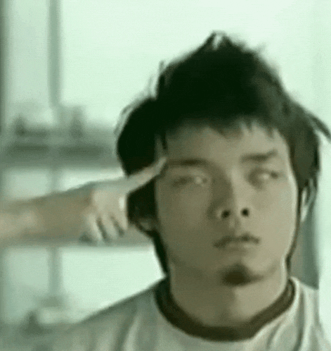 a man is getting his hair cut by a woman who is pointing at his head .