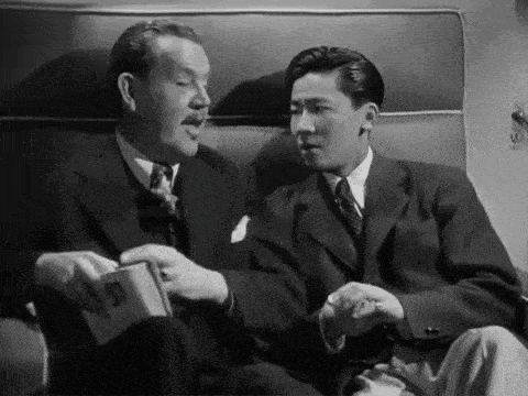 two men are sitting on a couch and one of them is holding a book