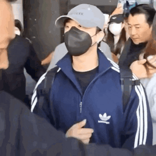 a man wearing a face mask and a hat is standing in a crowd of people .