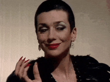 a woman with short hair and red nails is wearing a black fur coat .