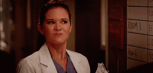 a woman in a lab coat and scrubs is standing in a hallway next to a whiteboard .