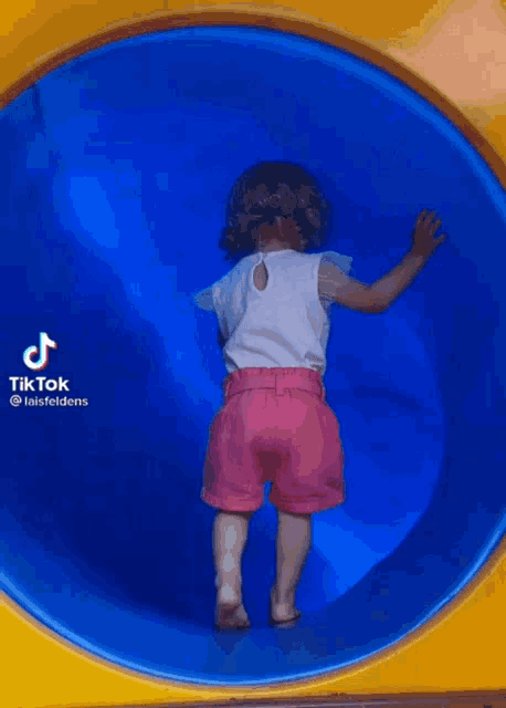 a little girl in pink shorts is standing in the middle of a blue tunnel .
