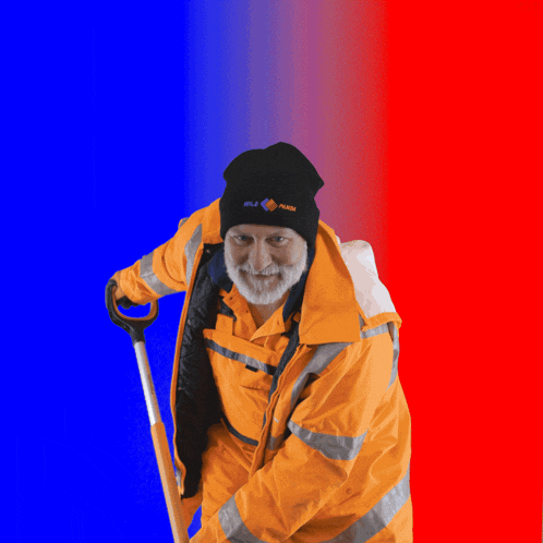 a man wearing an orange jacket and a black beanie with the word flash on it is holding a shovel