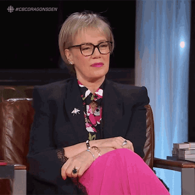 a woman wearing glasses is sitting in a chair with her legs crossed and the hashtag #cbcdragonsden above her