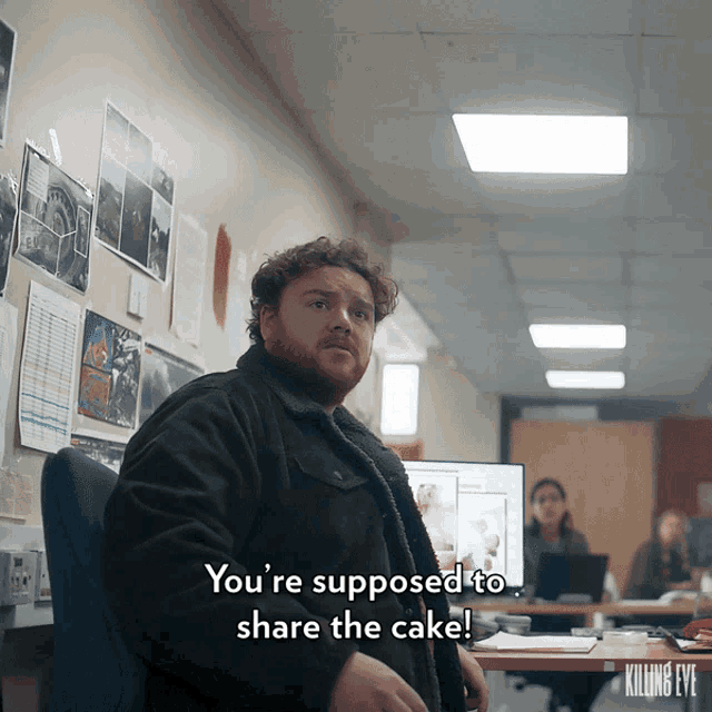 a man is sitting at a desk and says " you 're supposed to share the cake ! "