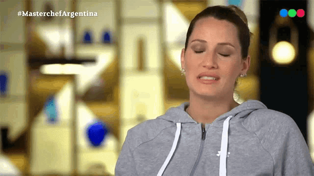 a woman wearing a grey hoodie is crying in front of a masterchef argentina advertisement