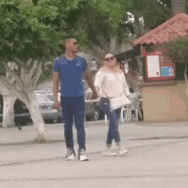 a man and a woman are walking down a sidewalk holding hands