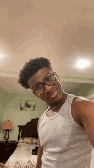 a young man wearing glasses and a tank top takes a selfie in a bedroom