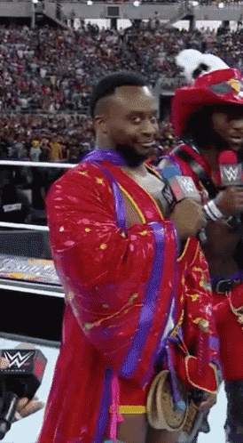 a man in a red and purple robe is talking into a microphone with a w logo in the background