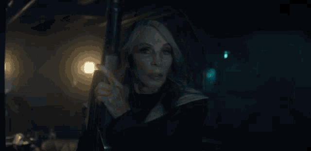 an older woman is holding a gun in a dark room and pointing at the camera .