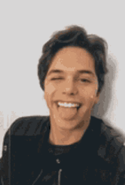 a young man in a black jacket is sticking his tongue out and smiling .