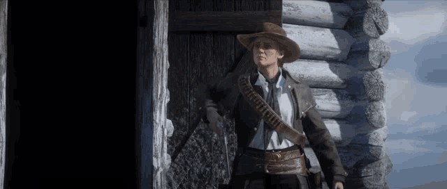 a woman in a cowboy hat is standing in front of a wooden cabin .