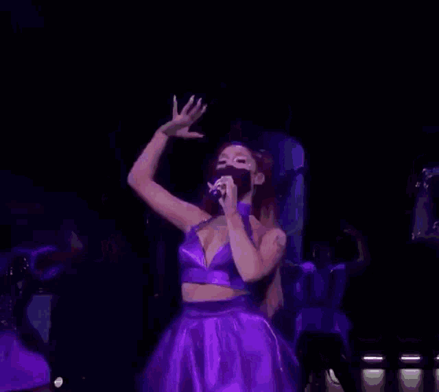 ariana grande is dancing on stage while wearing a purple dress and holding a microphone .