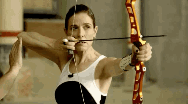 a woman in a white tank top is holding a bow and arrow in her right hand