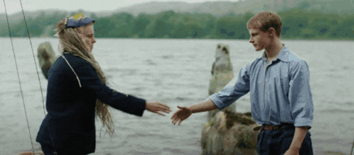 a man and a woman shake hands near a body of water