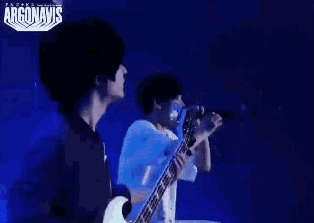 a man is playing a guitar and singing into a microphone on a stage in front of a blue background .
