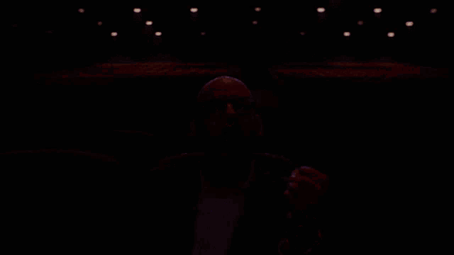 a bald man wearing glasses is sitting in an empty auditorium