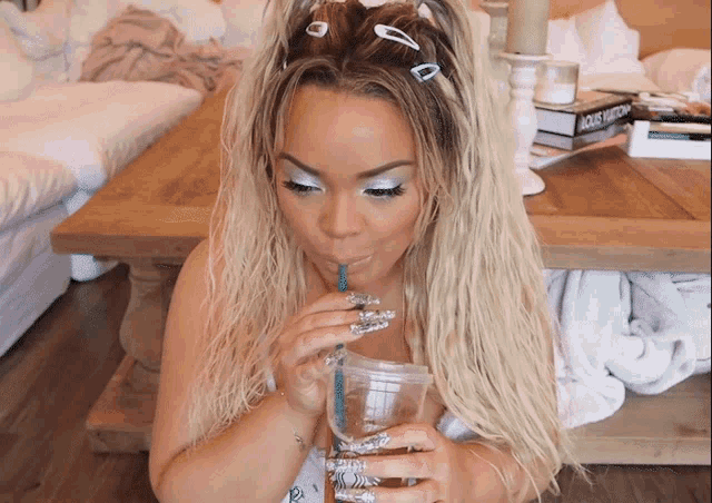 a woman drinking from a plastic cup with a louis vuitton book on the table behind her